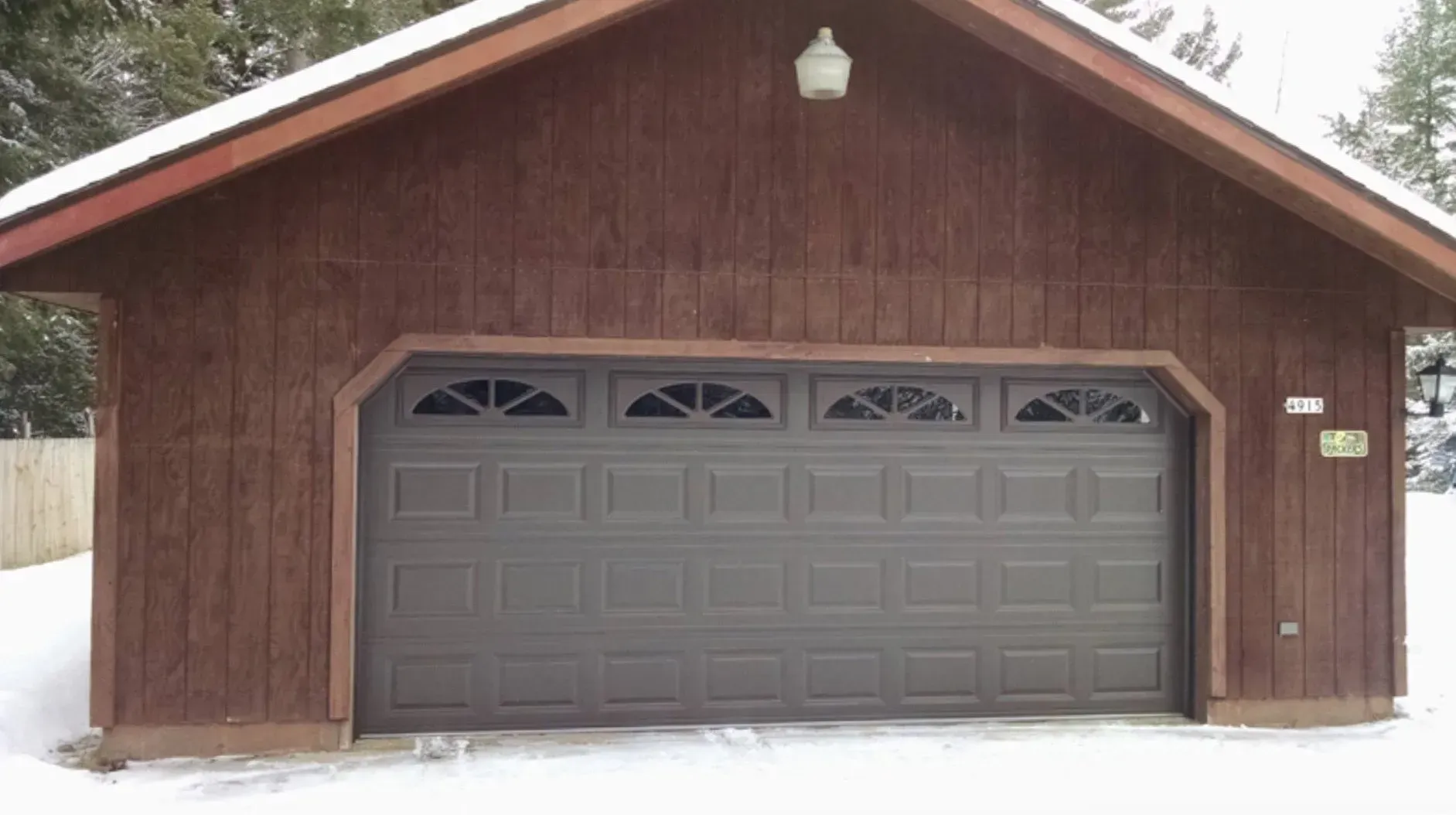 Brown garage with a gray garage door, snow on the ground.