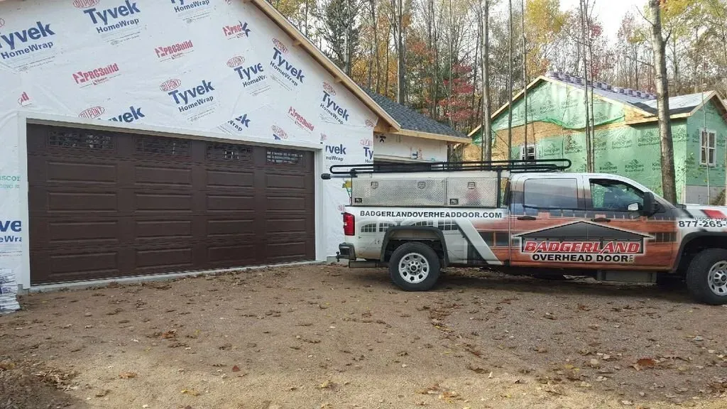 Brown garage door, white truck with logo parked next to a house under construction.
