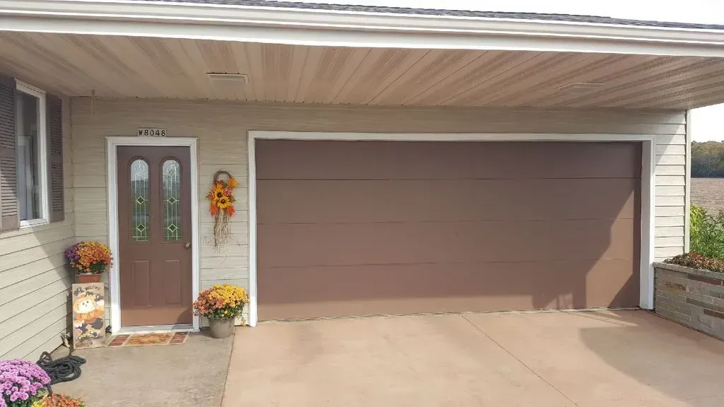 Brown garage door next to a brown door with a seasonal pumpkin decoration.