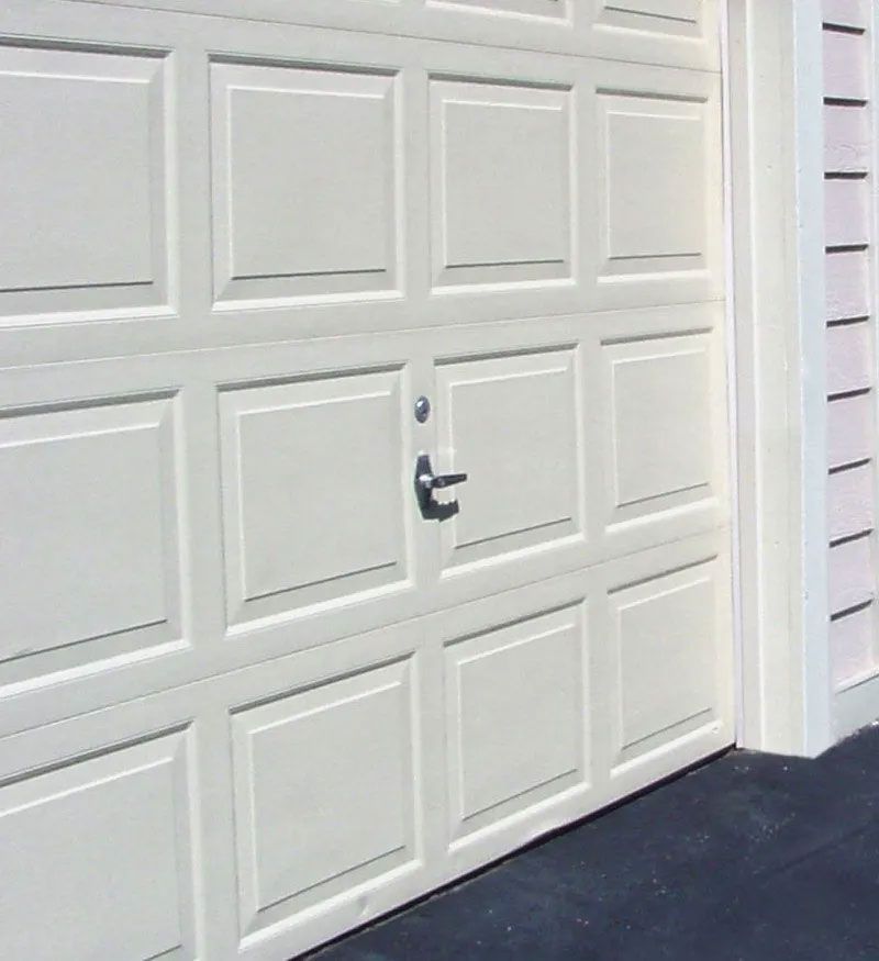 White paneled garage door with a handle, next to light-colored siding.