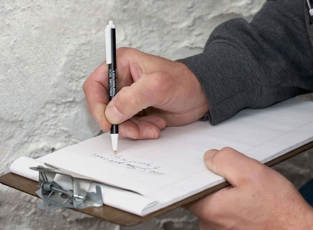Person writing on a clipboard with a pen in front of a stone wall.