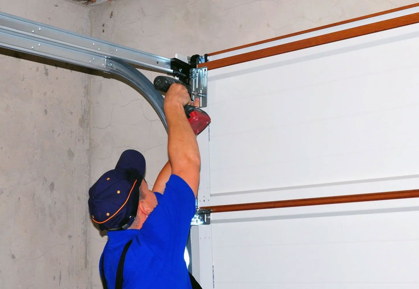 Person in blue shirt installing garage door track with a power drill.