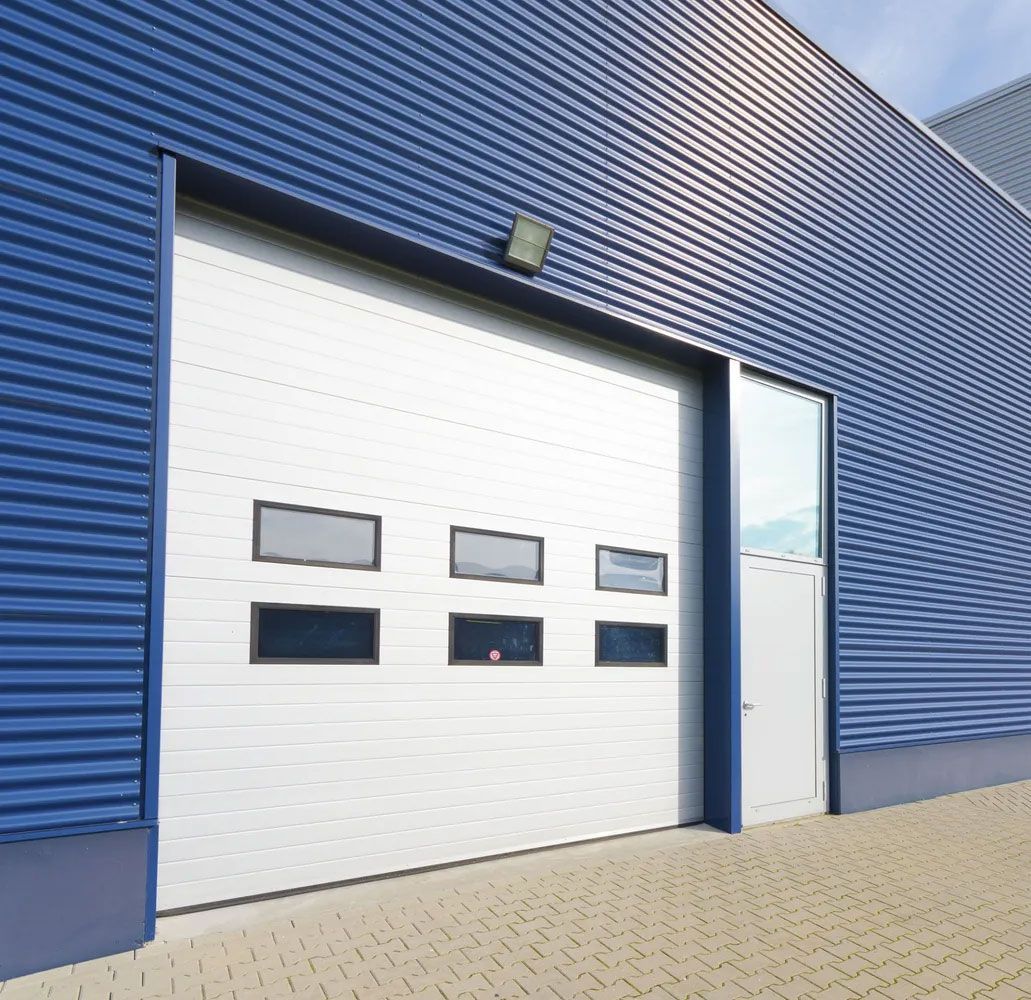 Blue industrial building with large garage door, glass windows, and a small door.