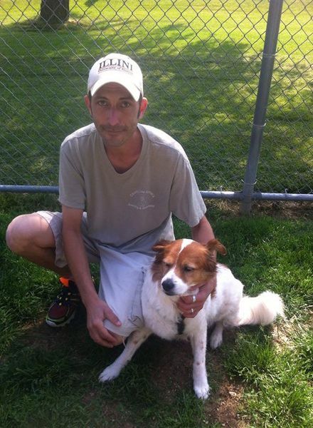 A man kneeling next to a dog wearing an illinois hat