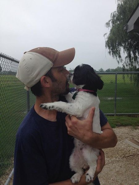 A man in a baseball cap is holding a black and white puppy