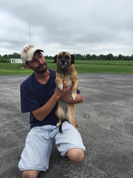 A man kneeling down holding a dog with a hat that says ' rangers ' on it