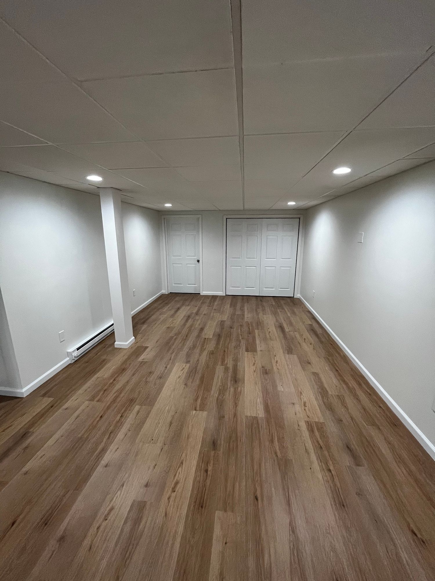 An empty basement with hardwood floors and white walls.