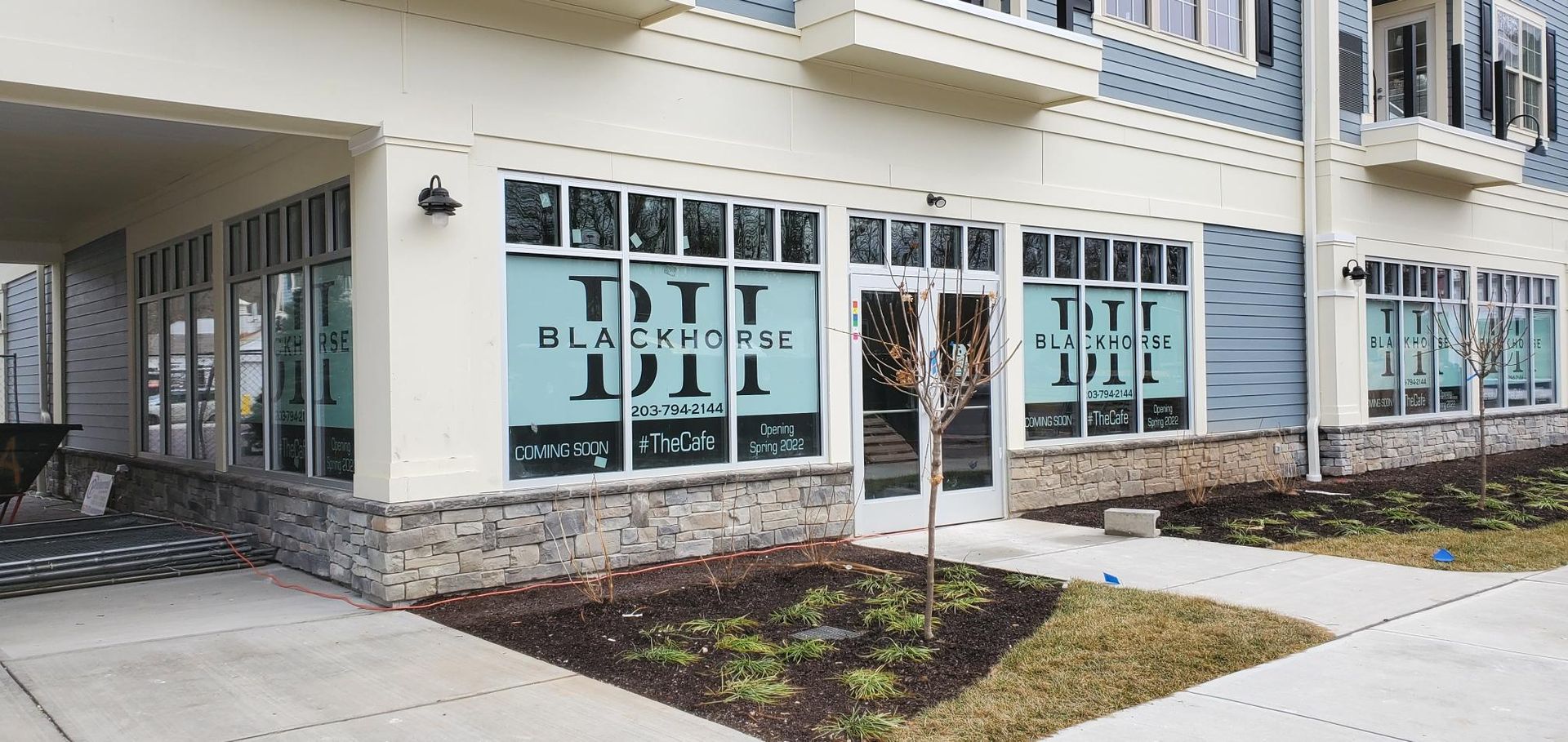 A street-level view of a commercial storefront with blue windows, tan walls, and stone trim on a building exterior.