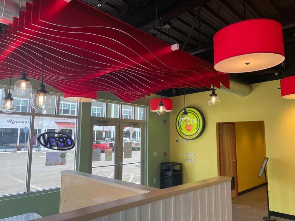 Interior of a brightly lit fast-casual restaurant featuring red acoustic ceiling waves and matching pendant lights.