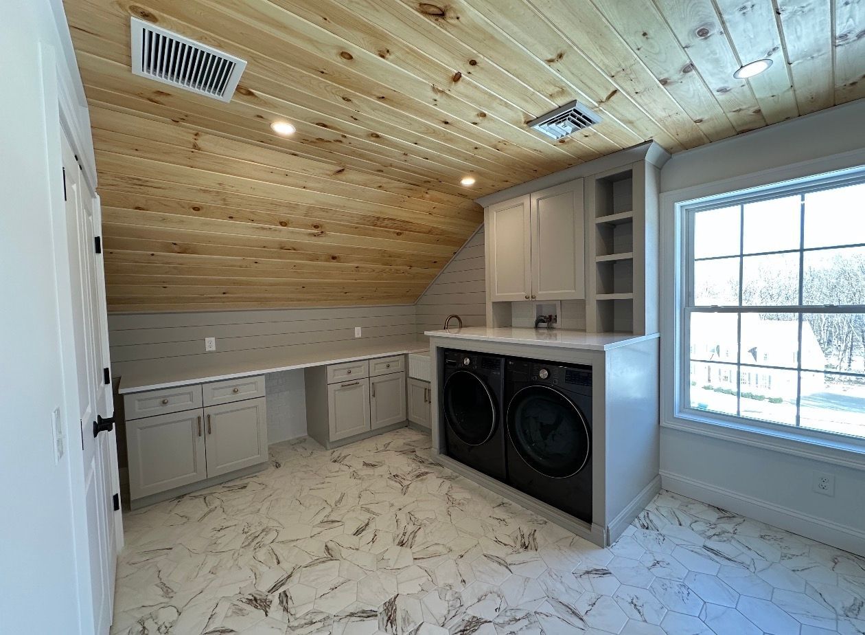 A laundry room featuring a wood-paneled ceiling, light gray cabinets, black front-load appliances, and marble-look flooring.