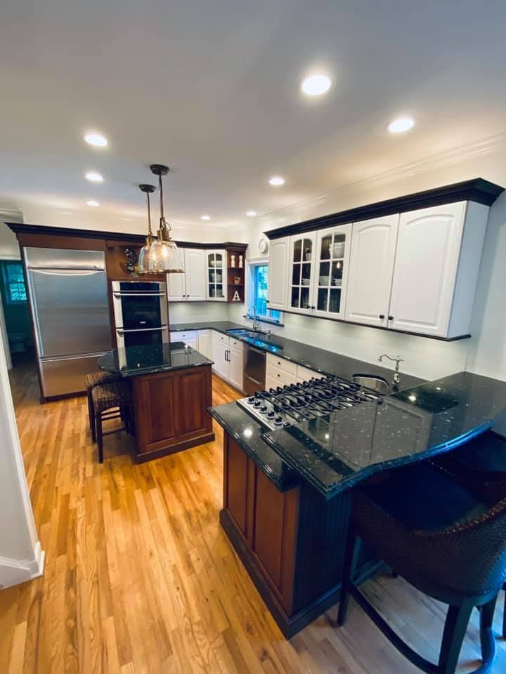 A kitchen with hardwood floors , white cabinets , stainless steel appliances and a large island.