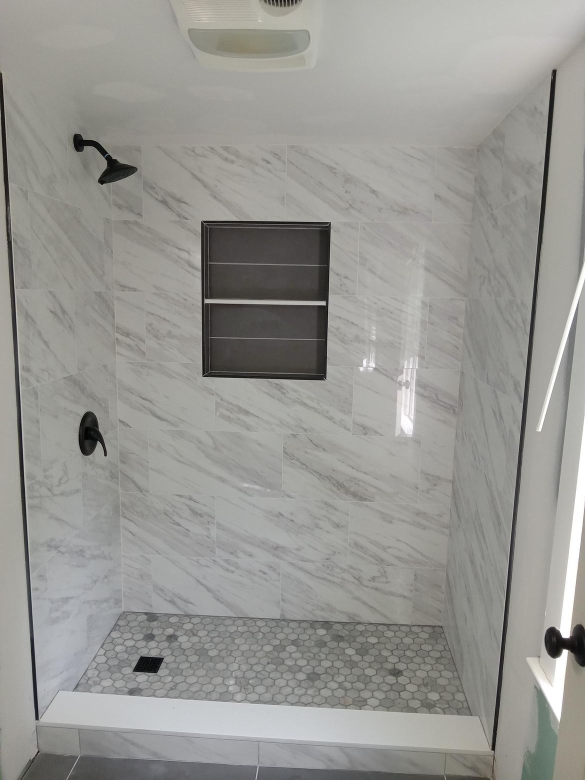 A shower stall with marble walls and a window.