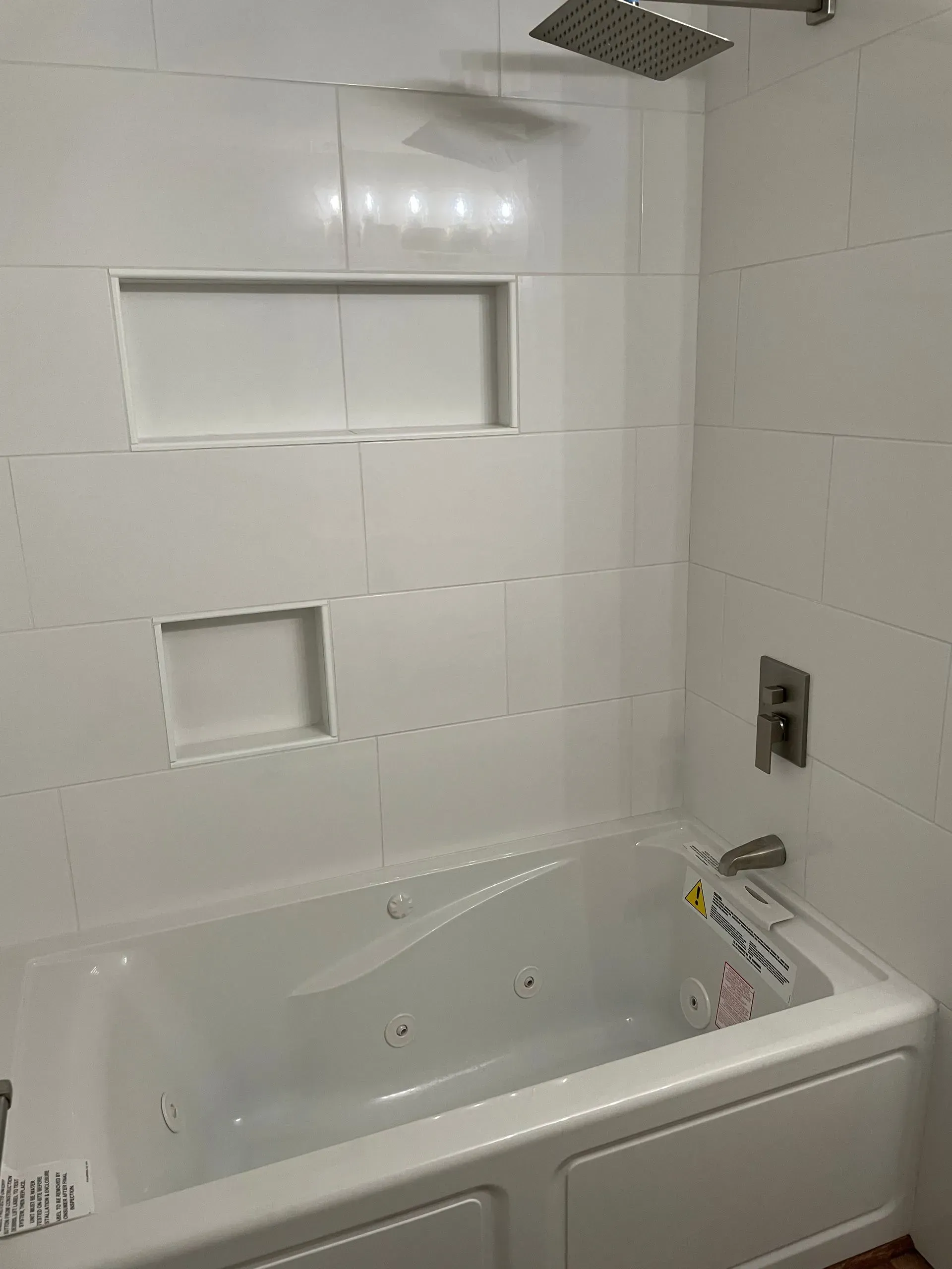 A clean white bathtub and shower surround with two recessed wall niches and modern stainless steel fixtures.