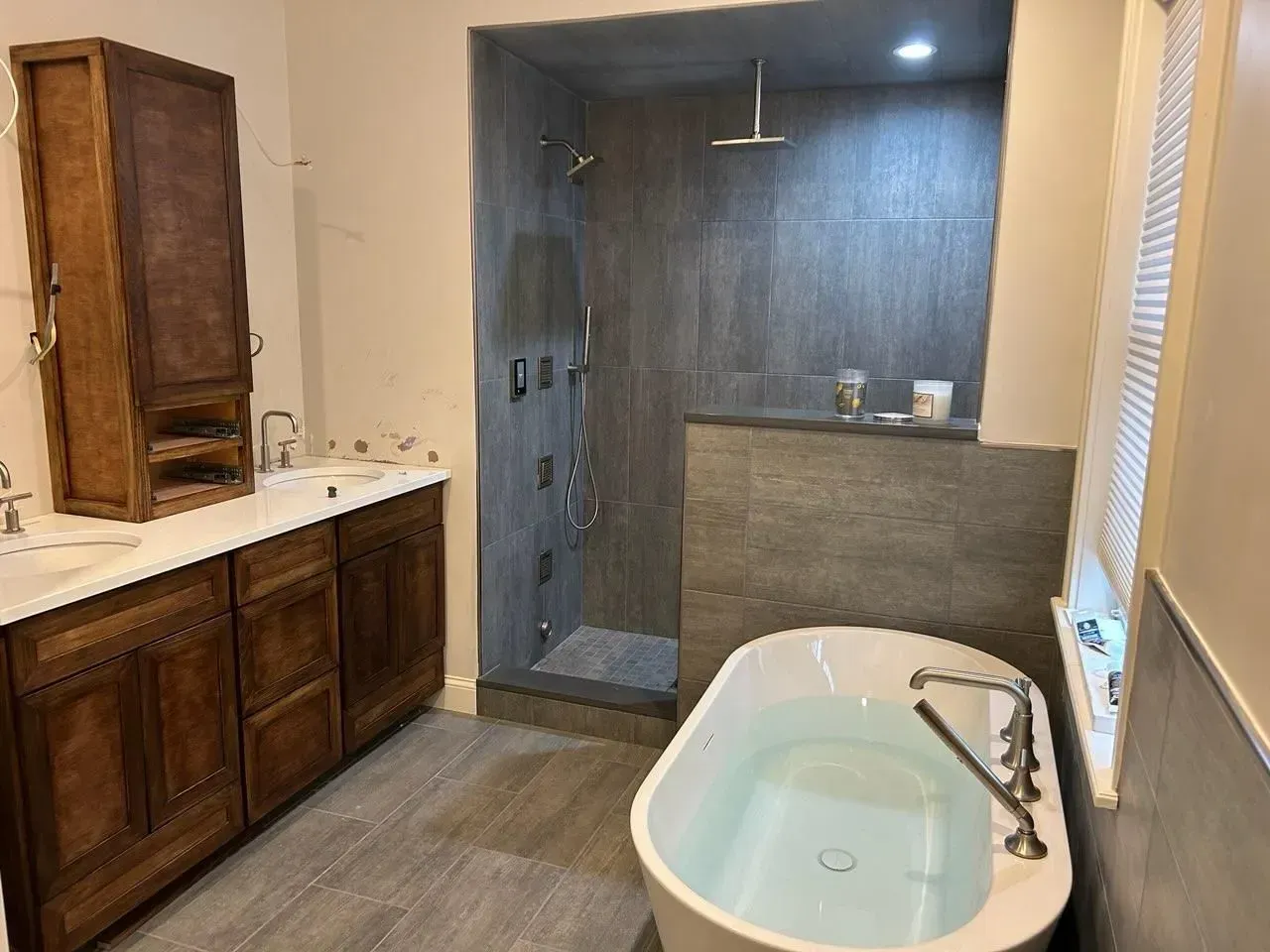 A bathroom with dark wooden cabinets, a soaking tub, and a walk-in shower with grey tiled walls.