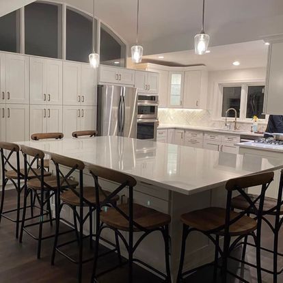 A kitchen with white cabinets , stainless steel appliances , a large island with a table and chairs.