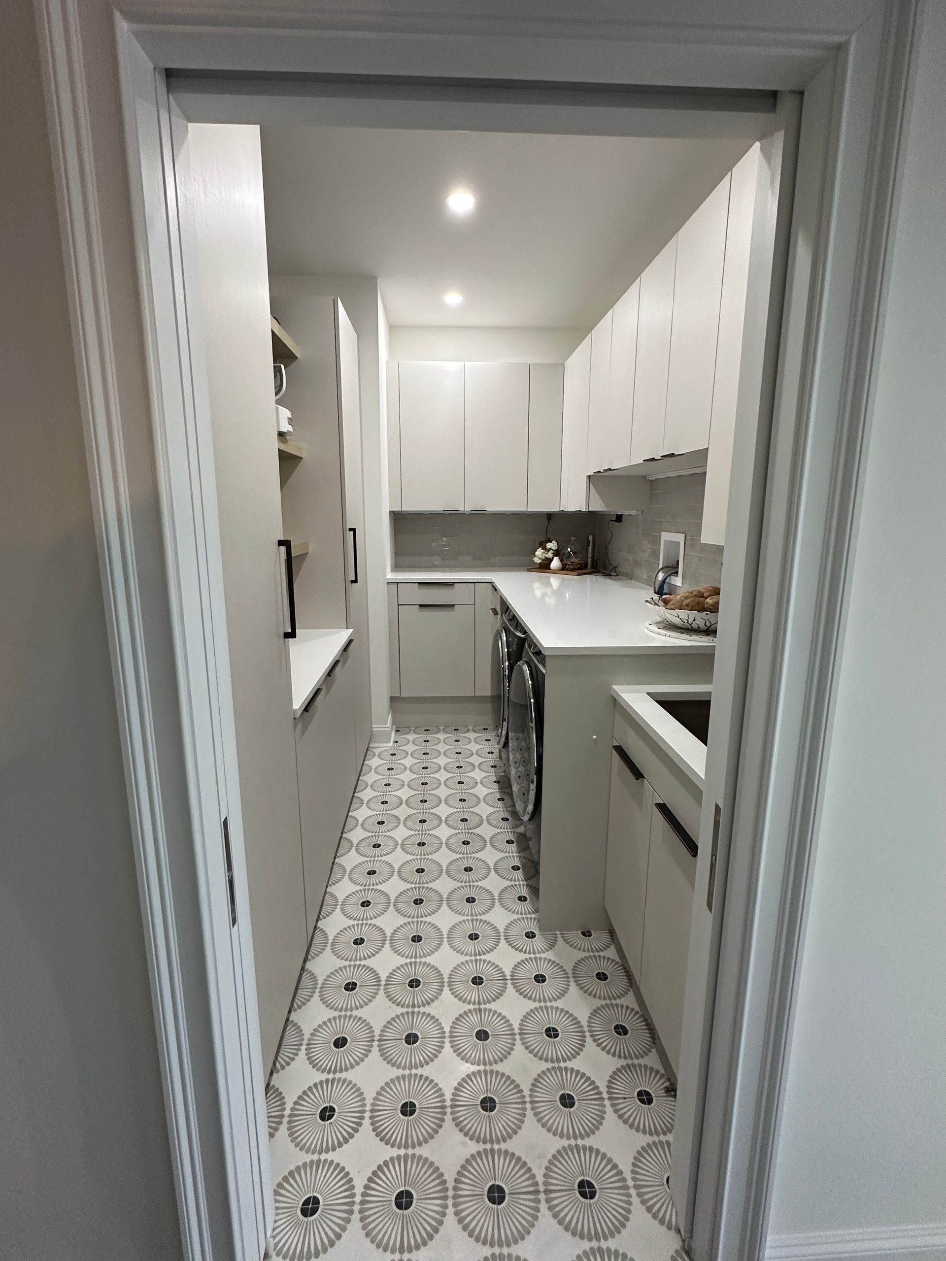 A kitchen with white cabinets and black and white tiles on the floor.