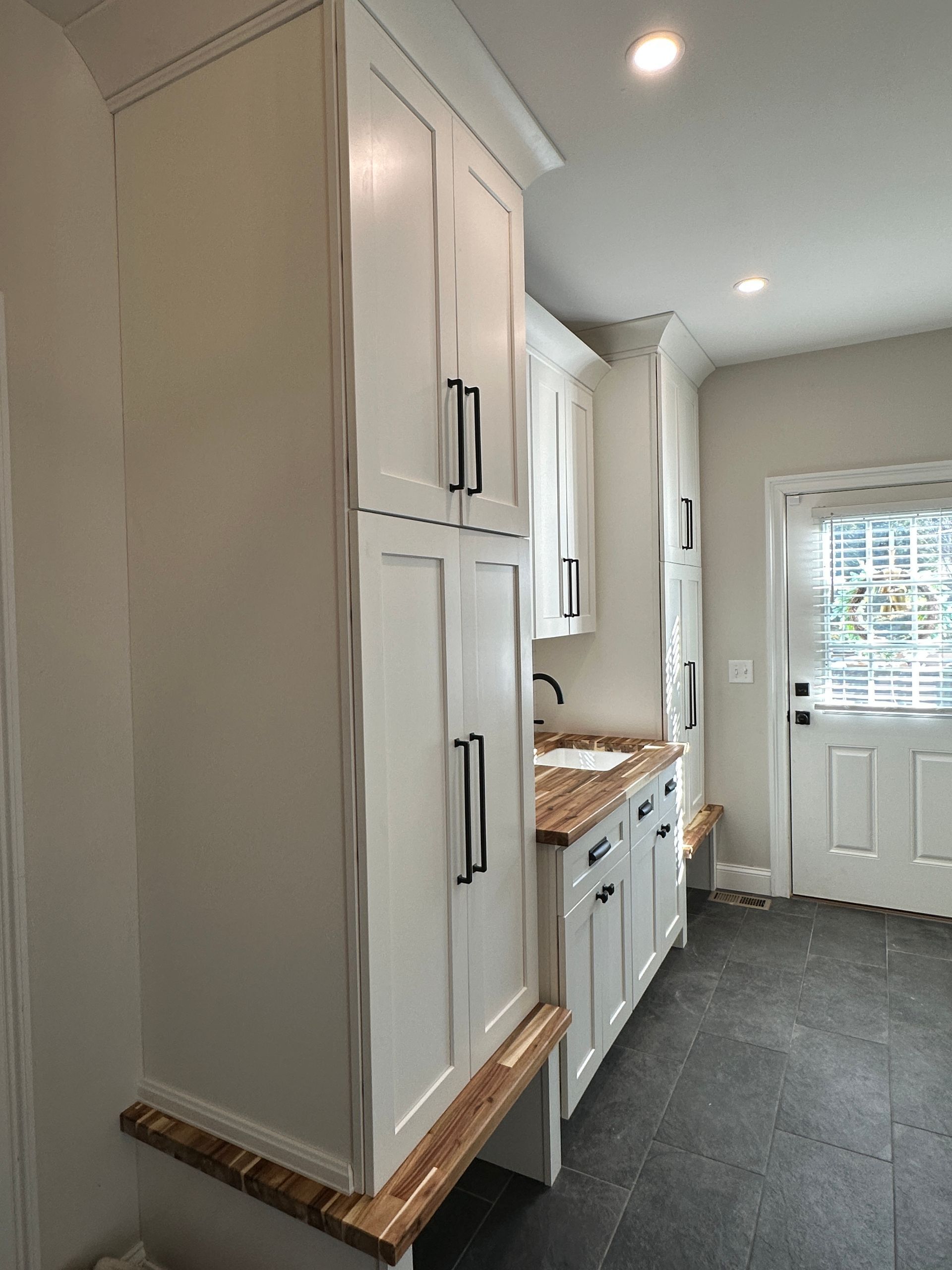 A laundry room with white cabinets and a sink.