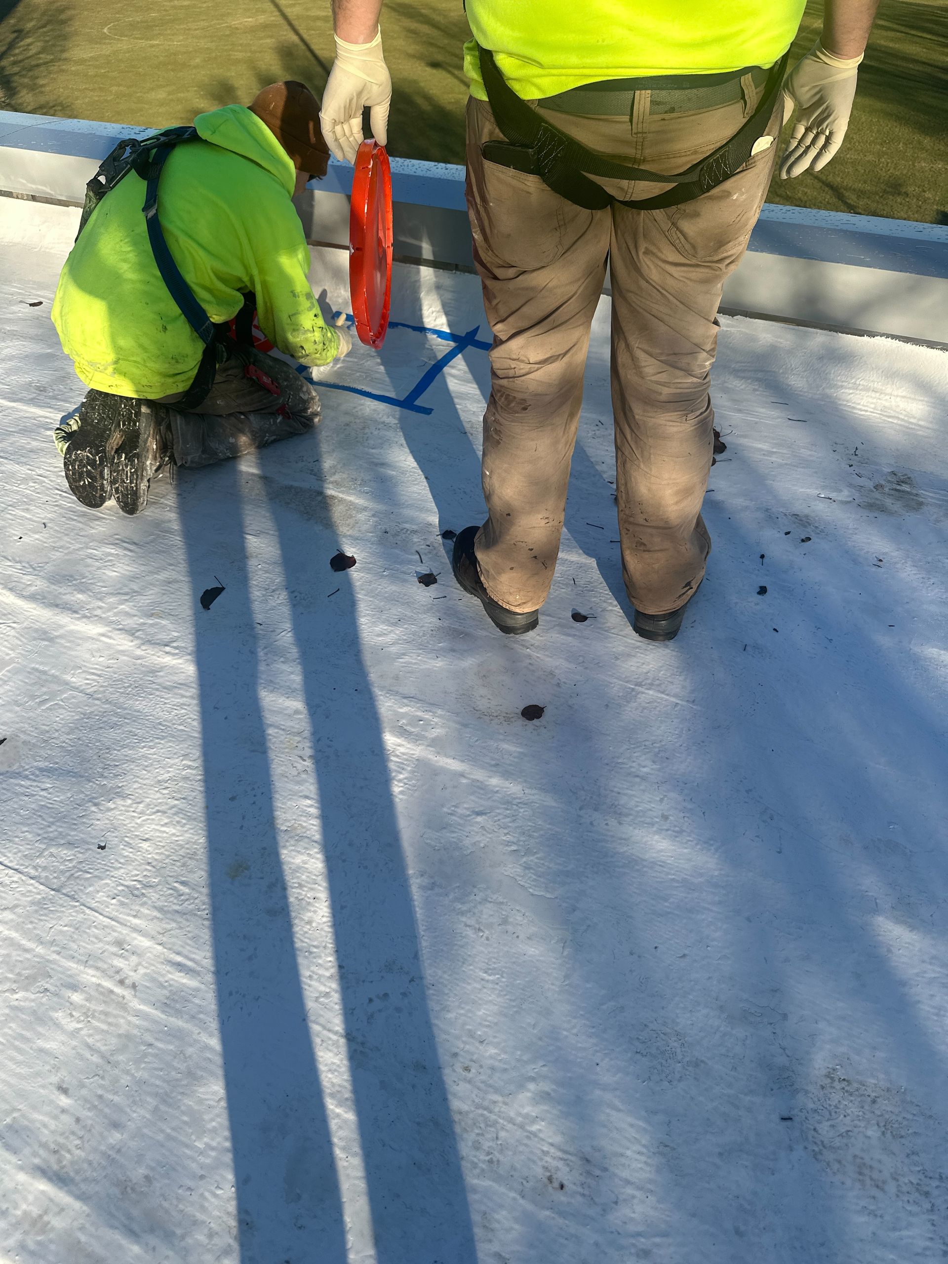 Two men are working on a roof and one is kneeling down.