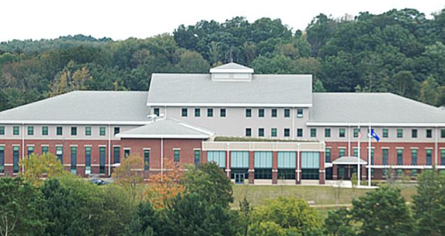 A large building with a gray roof is surrounded by trees