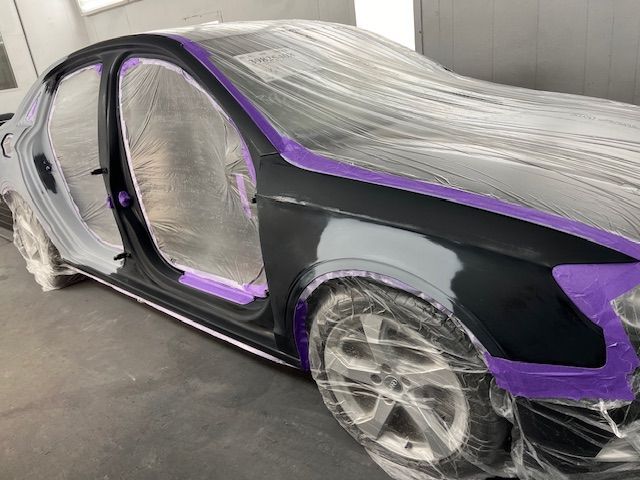 A black car is covered in plastic and purple tape.