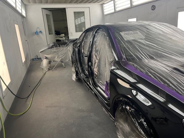 A black car is being painted in a paint booth.