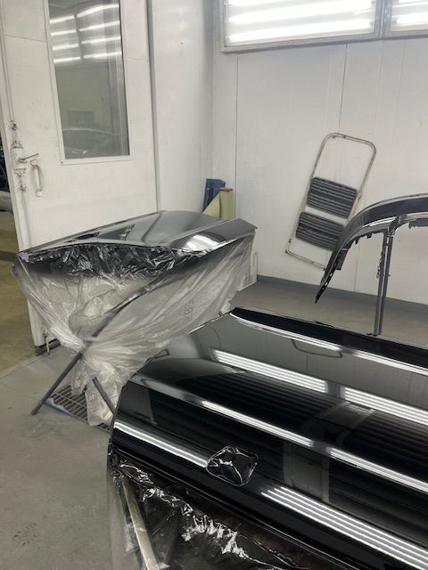 A black car is being painted in a paint booth.