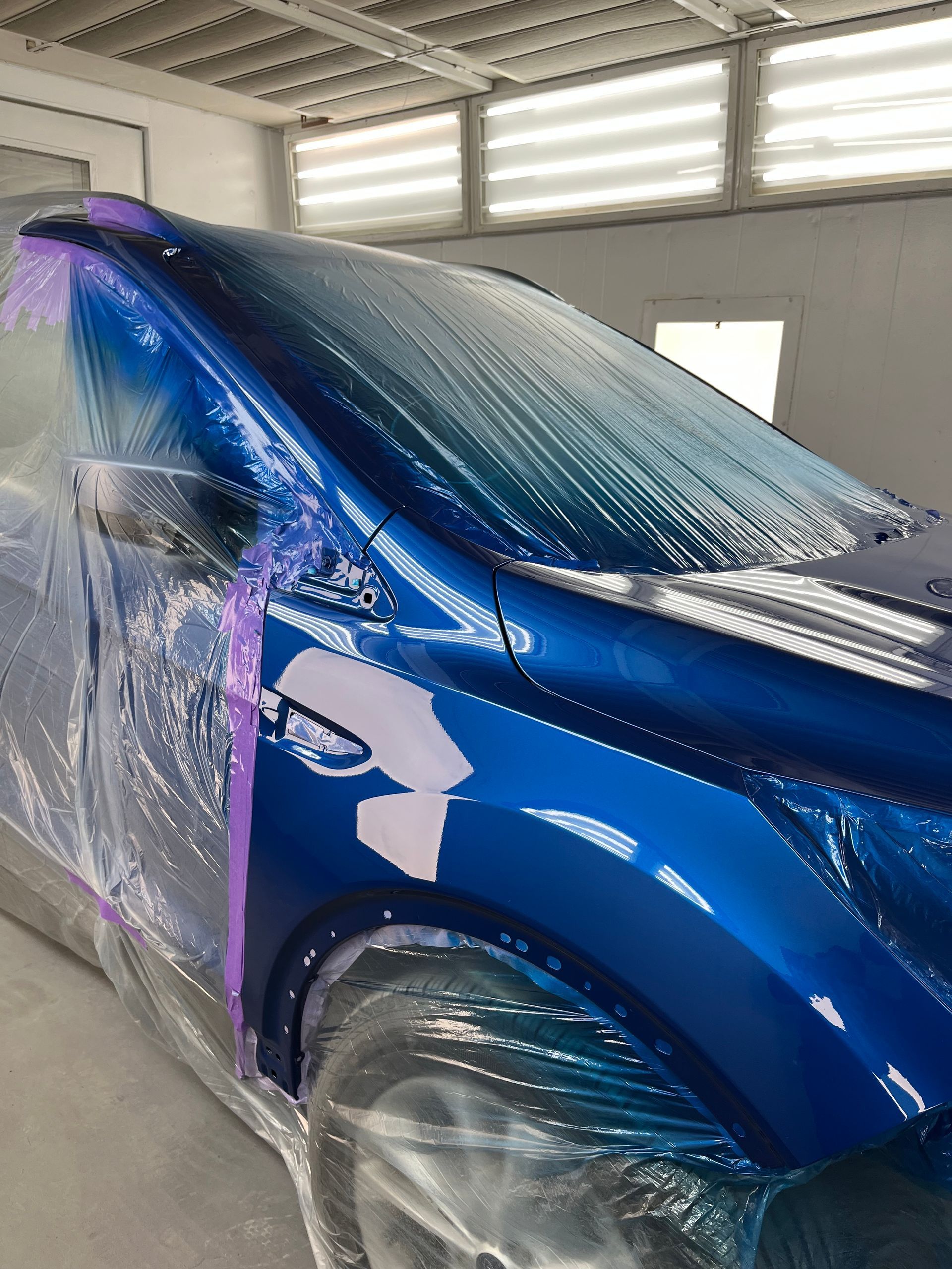 A blue car is being painted in a paint booth.