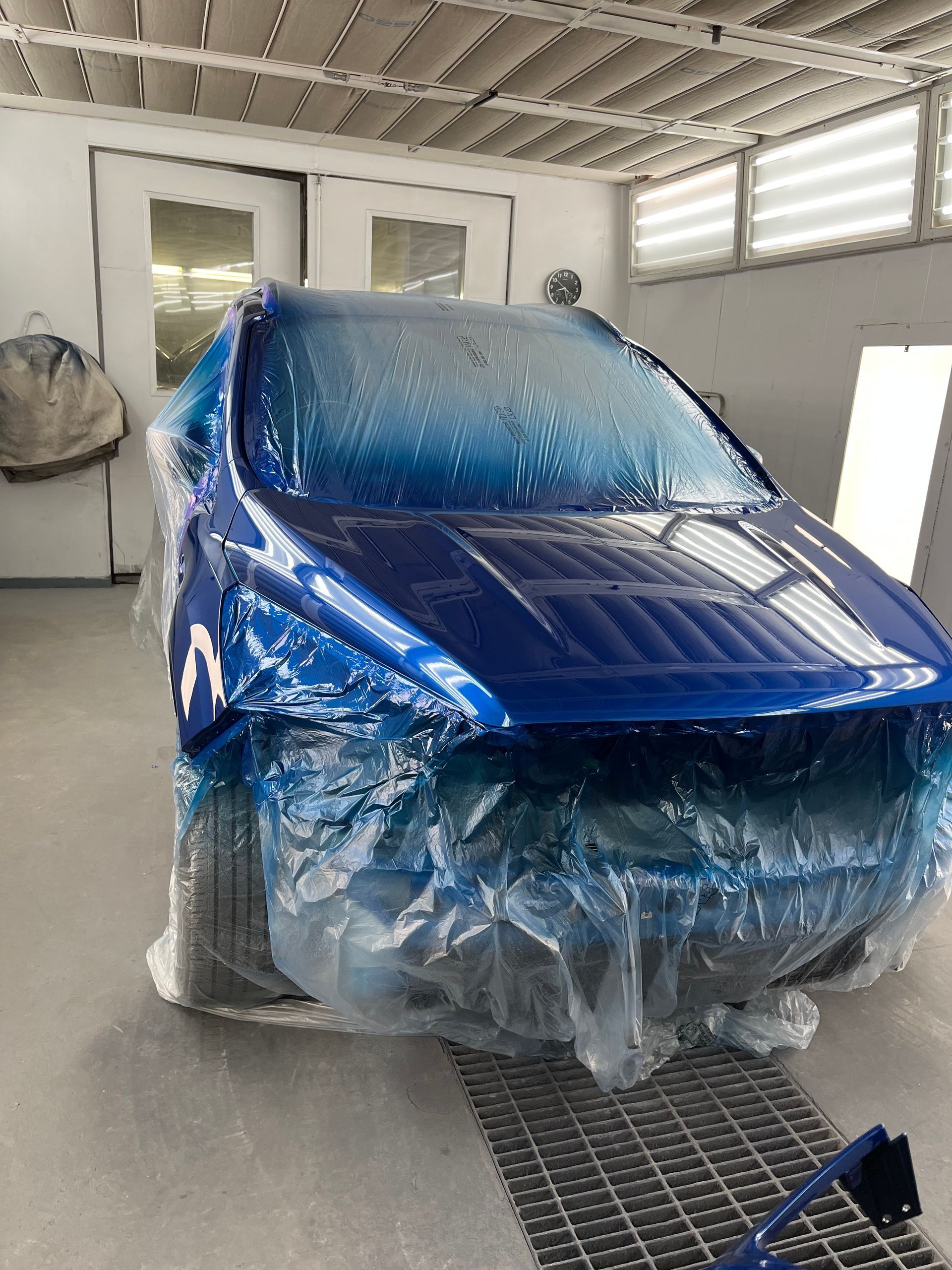 A blue car is wrapped in plastic in a paint booth.