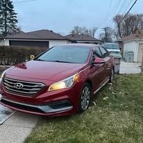 A red car is parked on the side of the road in front of a house.