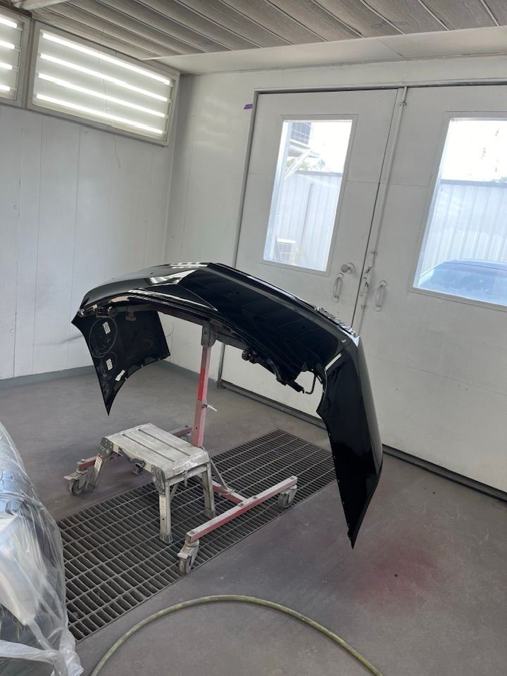 A black bumper is sitting on a stand in a paint booth.
