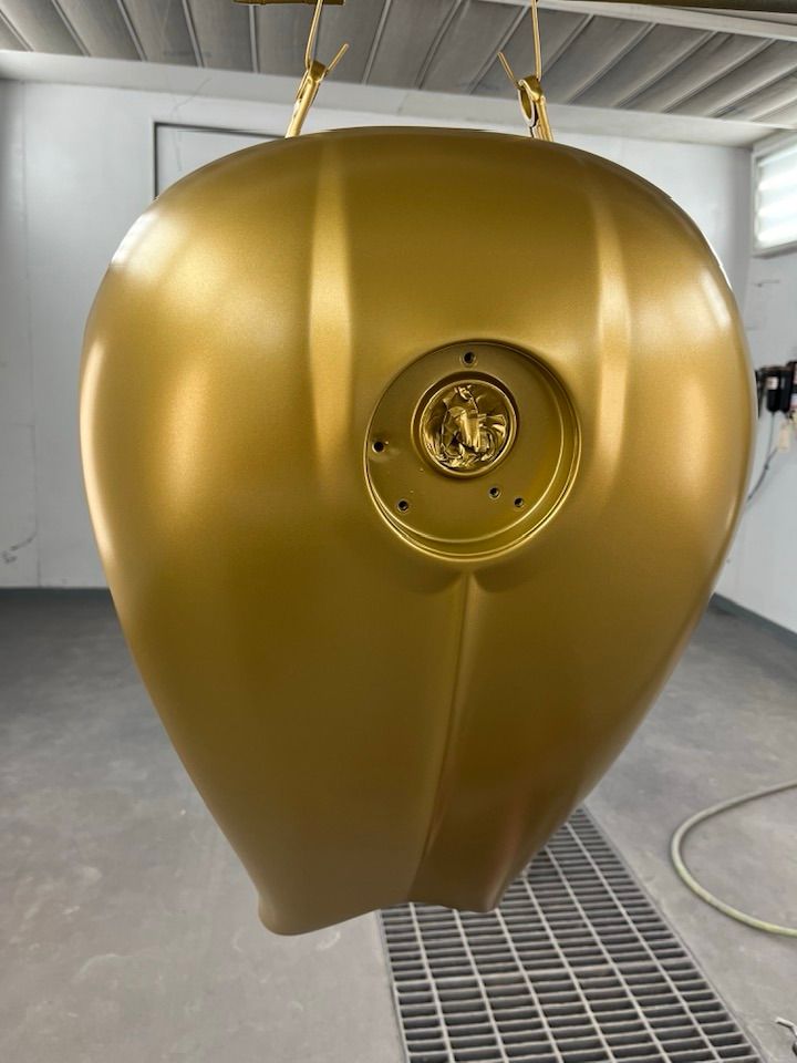 A gold motorcycle tank is hanging from the ceiling in a garage.