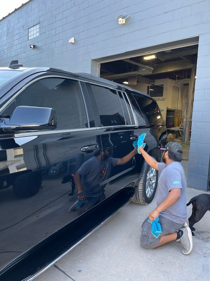 A man is kneeling down next to a black suv in front of a garage.