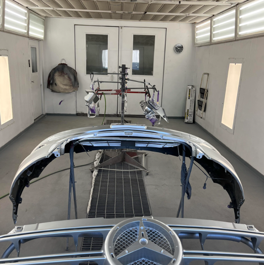 A mercedes bumper is being painted in a paint booth.
