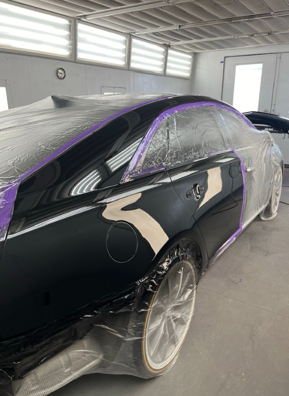 A black car is being painted in a garage.