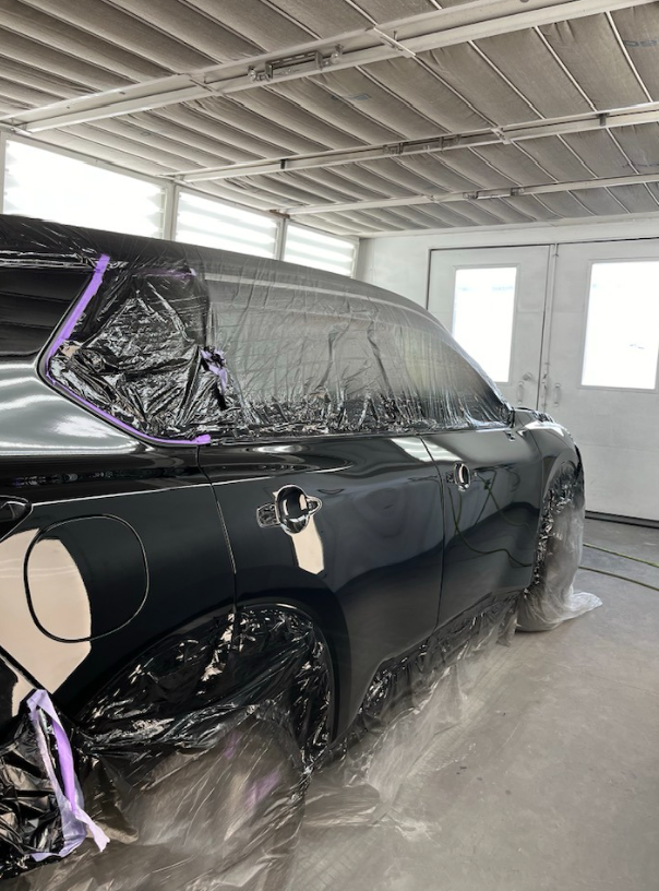 A black car is being painted in a garage.