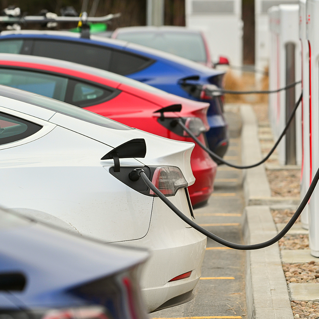Electric cars charging at a station; white, red, and blue vehicles.