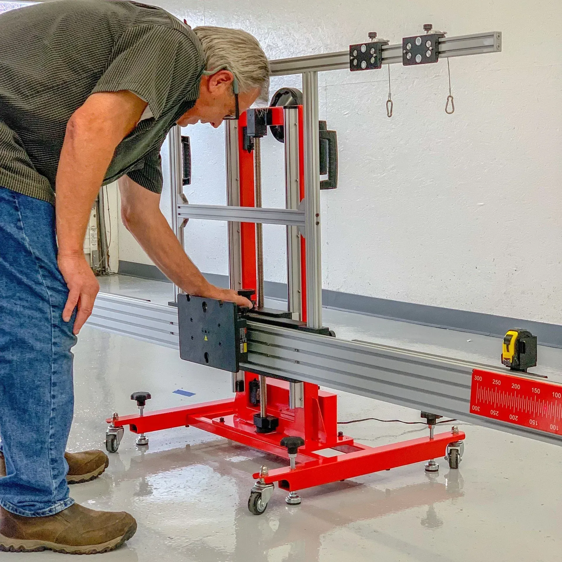 Man uses a red measuring machine in a workshop. He is looking down at it, with a tape measure nearby.
