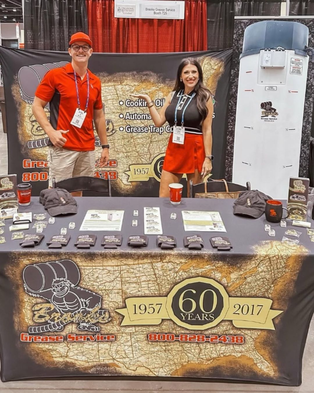 Two people at a trade show booth with merchandise. The booth features a map design.