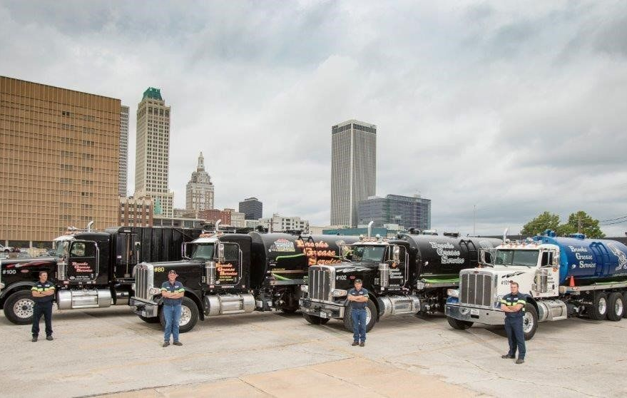 Several black trucks with workers in front, city skyline background.