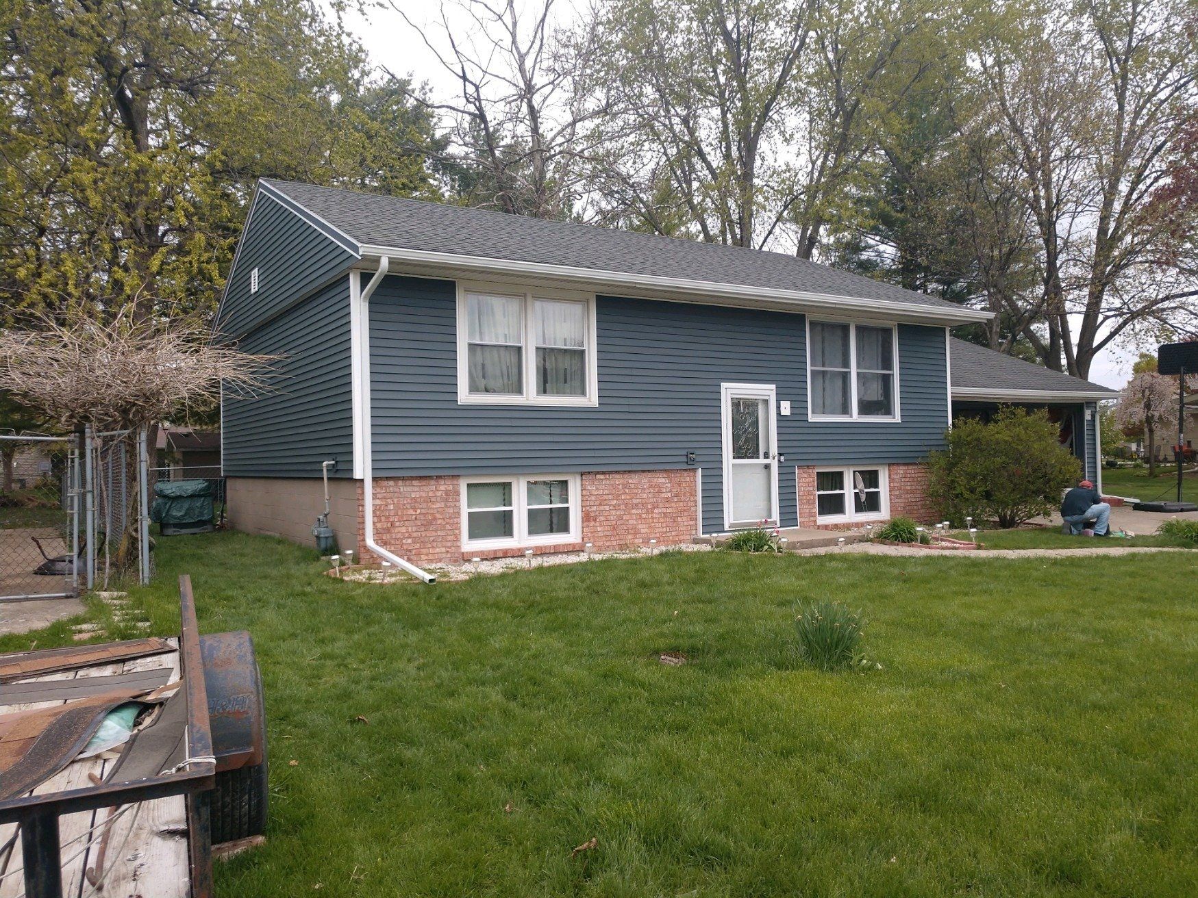 A house with a blue siding and a brick foundation is sitting on top of a lush green lawn.