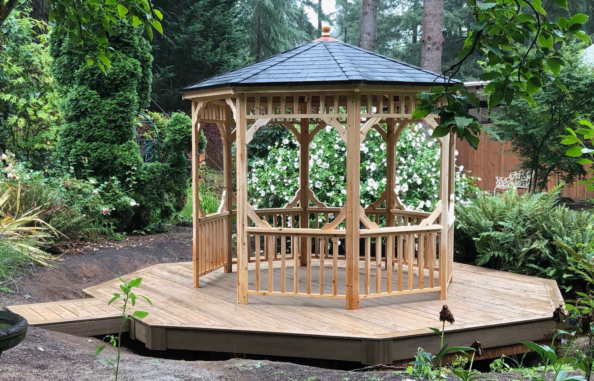 A wooden gazebo is sitting on a wooden deck in the middle of a forest.