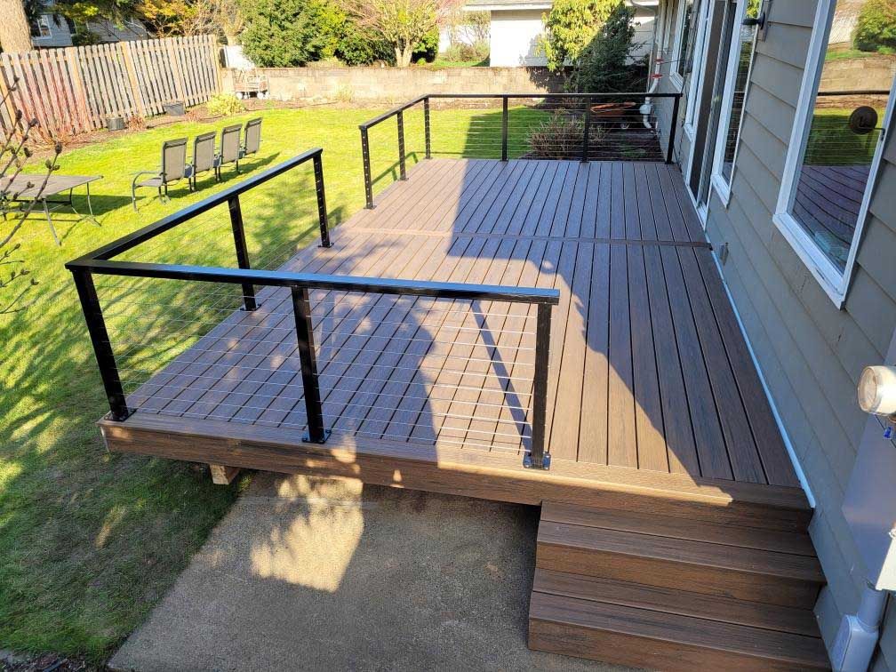 A wooden deck with stairs and a black railing is in the backyard of a house.