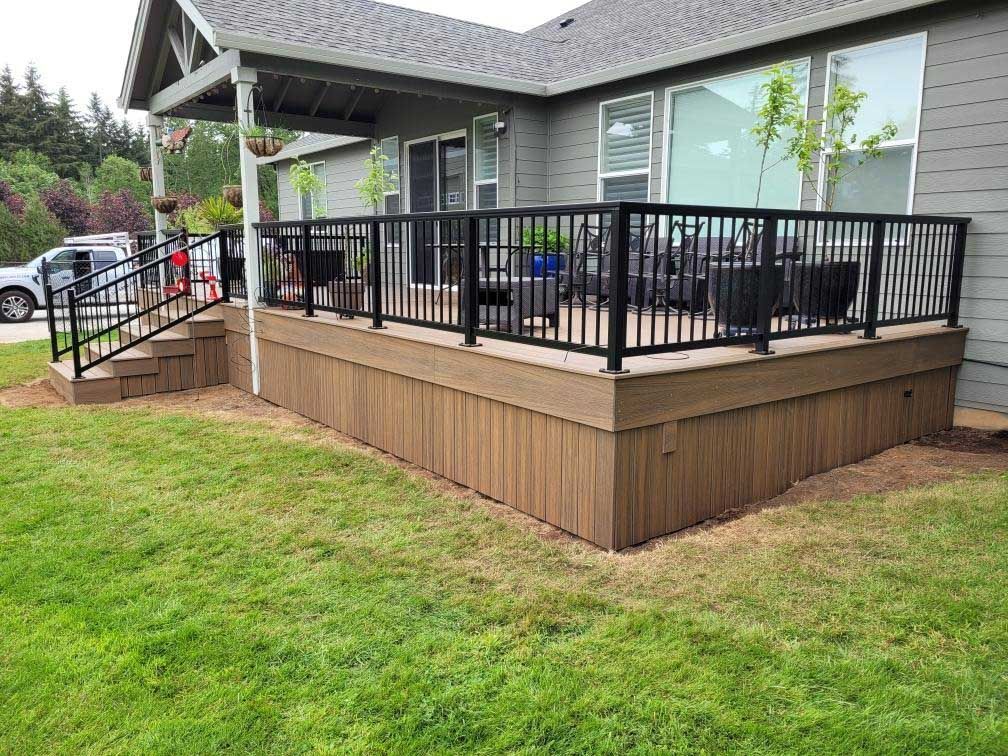 A wooden deck with a black railing is in front of a house.