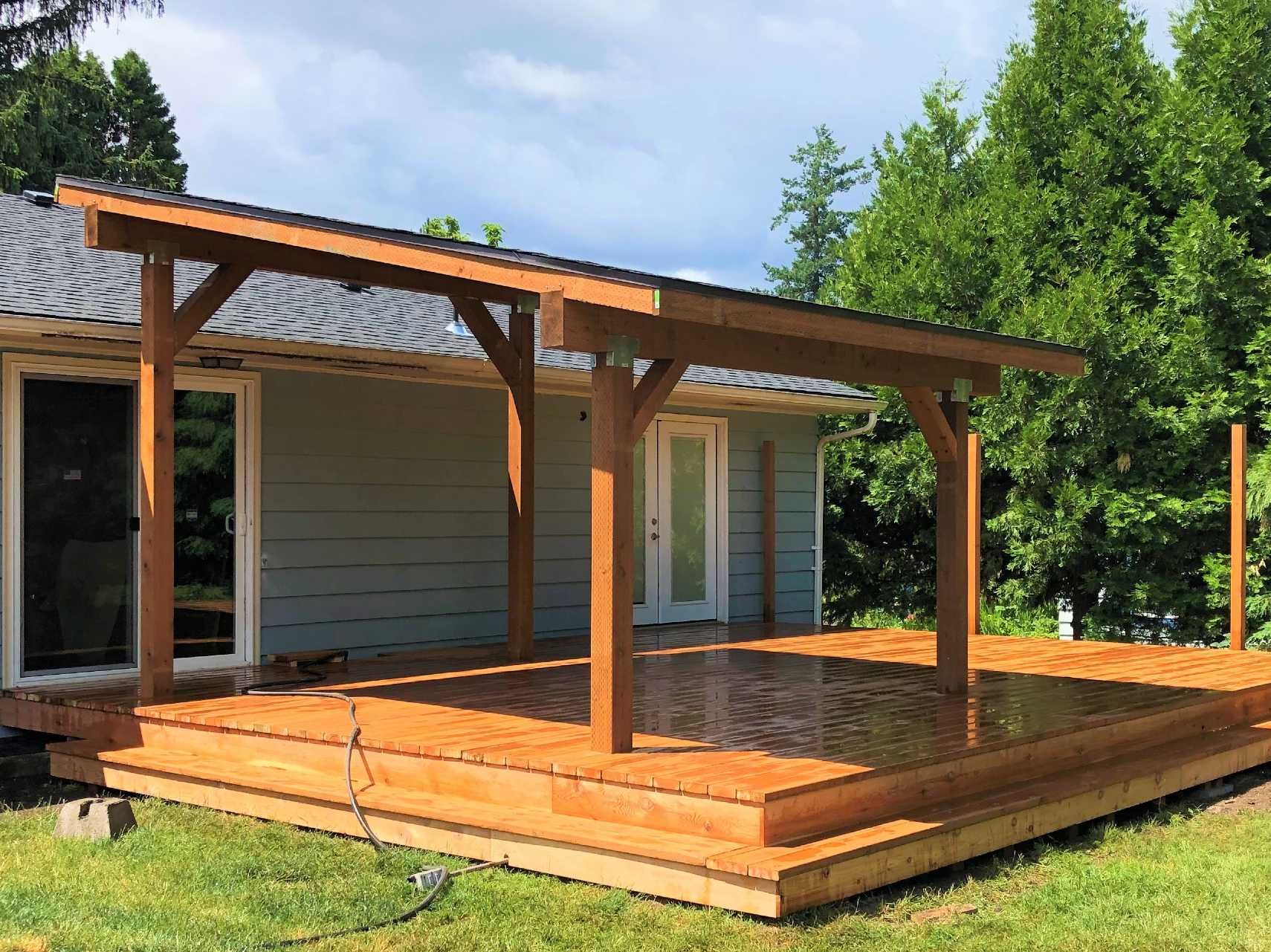 A wooden deck with a roof over it is in front of a house.