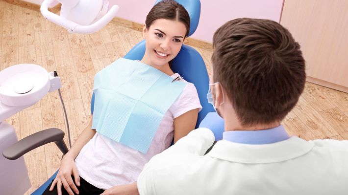 A woman is sitting in a dental chair talking to a dentist.