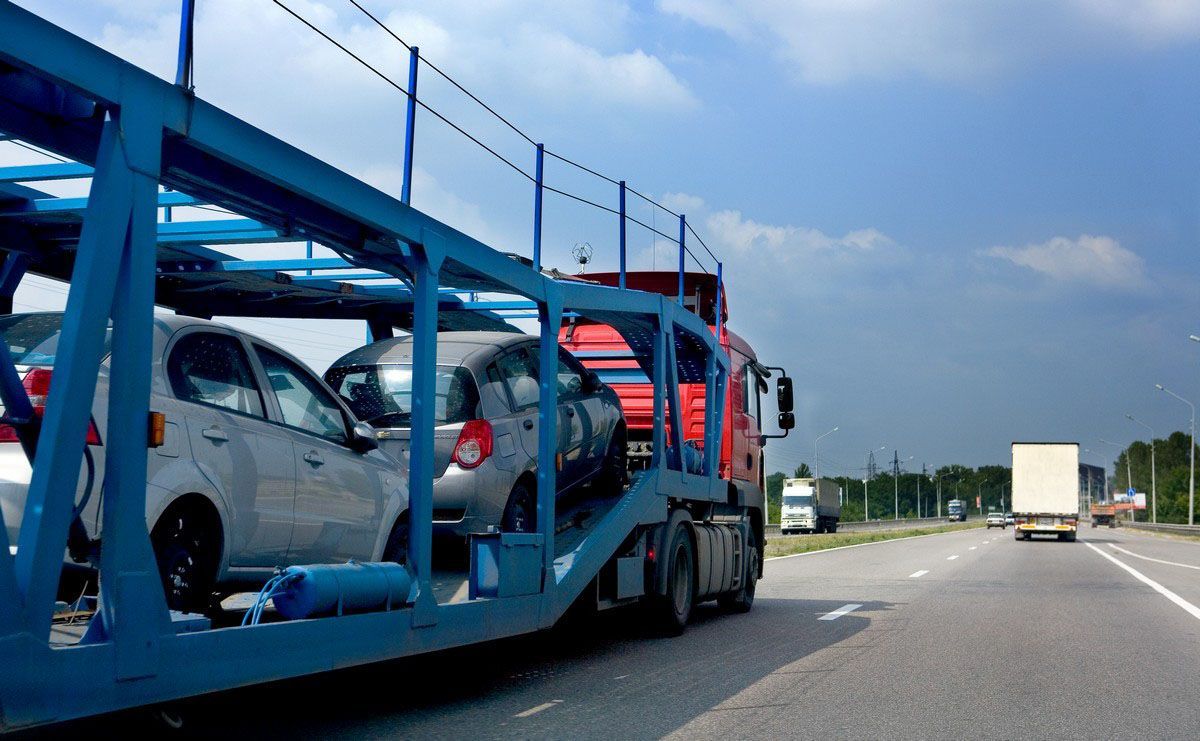 A red car carrier truck transporting silver hatchbacks along a highway under a blue sky.