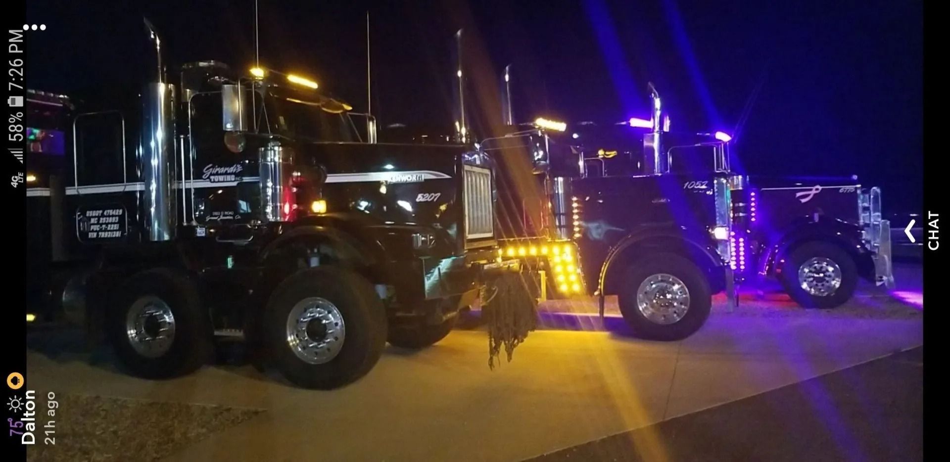 Three black, customized semi-trucks parked in a line at night, illuminated by bright headlights and colored LED accents.