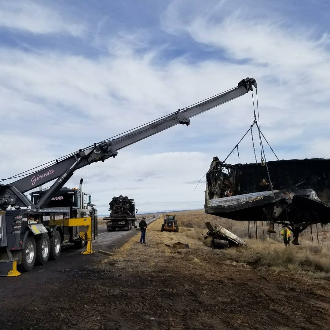 Large crane lifting a dark, burnt-looking vehicle in an open field under a cloudy sky