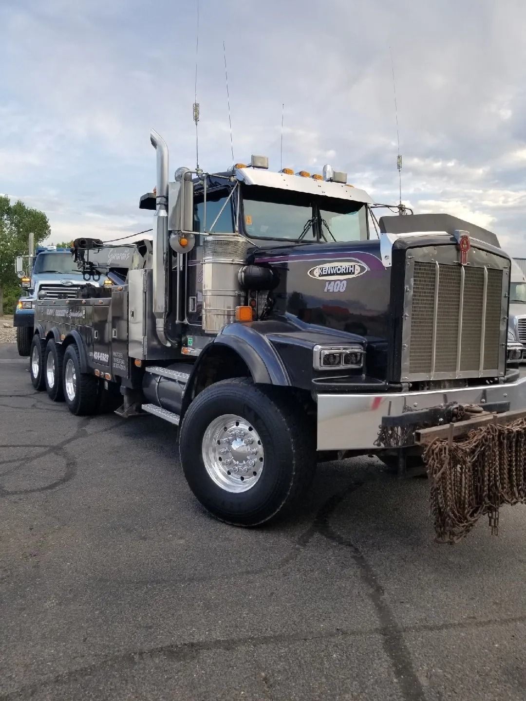 A dark purple Kenworth heavy-duty tow truck with chrome accents and a chain-link grill parked on an asphalt lot.