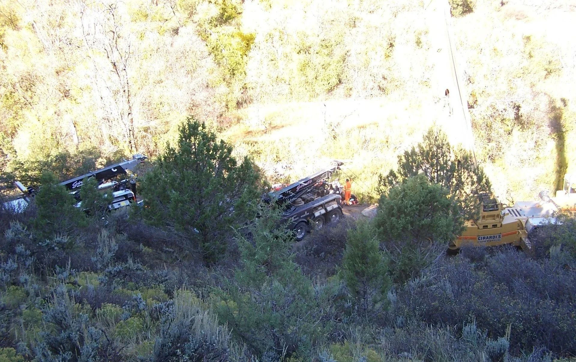 A yellow piece of construction equipment sits in a brush-covered area near a rocky slope with debris scattered around.